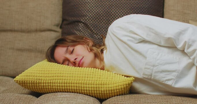 Tired young woman lying down to sleep on pillow on sofa at home. Girl feel exhausted, lack of energy, overwhelmed
