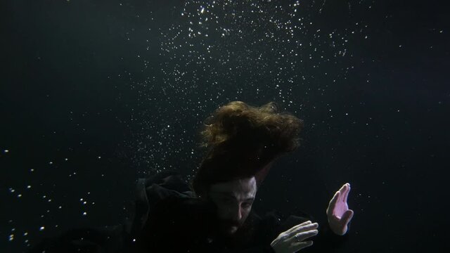 enigmatic handsome man with long hair is swimming in depth of sea or lake, underwater