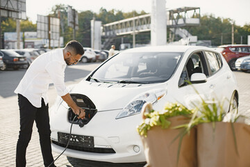 Young Arab man recharging white electric car