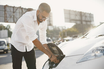 Young Arab man recharging white electric car