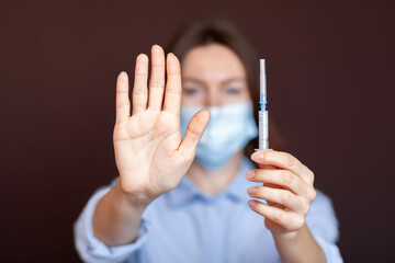 Coronavirus concept. Girl wearing mask for protection from disease and show stop hands gesture for stop corona virus outbreak. Stop the pandemic with vaccination. There is a syringe in the girl's hand