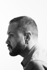 Emotive profile portrait of bearded charismatic muscular 40 years old man sitting over white background. Short haircut. Black and white studio shot. Text space