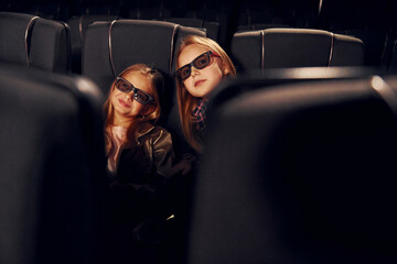 Two kids sitting in cinema and watching movie together