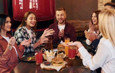 Having a conversation with each other. Group of young friends sitting together in bar with beer