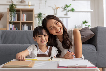 Happy asian young mother smile with daughter in living room at home. Asian young mother teaching small daughter to drawing reading and writing to develop her daughter skill. Home School Concept