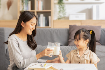 Asian mother and her daughter clink glasses enjoy and smile with milk drink.Mom and little girl holding milk glasses and drink to get calcium.Healthy Eating Concept