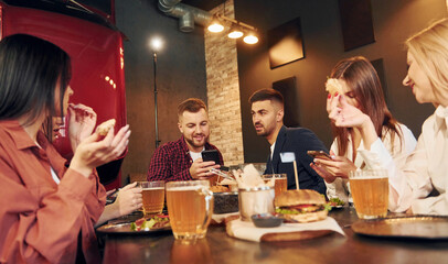 Weekend time spending. Group of young friends sitting together in bar with beer