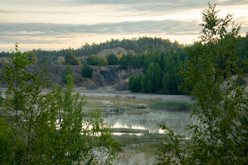 Fototapeta na wymiar Early morning in an abandoned flooded clay quarry. Beautiful clouds, steam above the water.