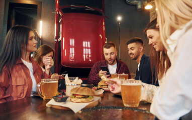 Modern interior. Group of young friends sitting together in bar with beer