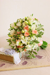 Bouquet of white freesia flower, pink roses and leaves and book on light pink background. Handle with peach colored ribbon. Bunch of flowers, vintage style, front view, vertical photo.