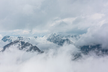 Naklejka na ściany i meble Awesome aerial view to high snowy mountains in dense low clouds. Minimal landscape with beautiful mountain peaks in thick clouds. Simple minimalism with snow mountain tops in cloudy sky above clouds.