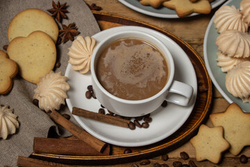 Cup of coffee on a wooden table. Coffee with milk, next to cookies and meringues. Coffee with dessert.