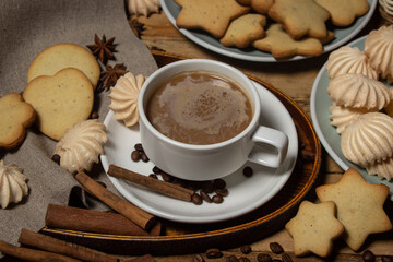 Cup of coffee on a wooden table. Coffee with milk, next to cookies and meringues. Coffee with dessert.