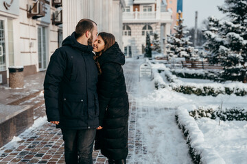 Fototapeta na wymiar Happy guy and girl walk through the snow-covered city and smile tenderly at each other