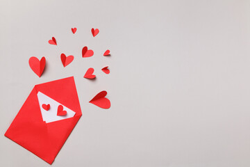 Red paper envelope with a white note inside and hearts on a gray pastel background. Love letter for Valentine's Day. Flat lay, top view.