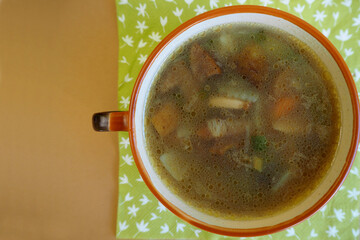 mushroom soup with Polish mushrooms, carrots, potatoes and onions in a brown plate is on a brown table. top view