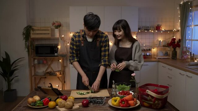 Zoom Out Of A Happy Asian Young Couple Working Together Making Valentine’s Day Dinner In A Cozy Decorated Kitchen At Home