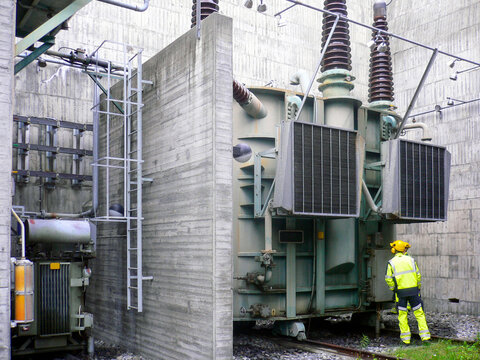 Engineer in yellow protective clothing, inspecting high voltage gear outside hydro power plant.