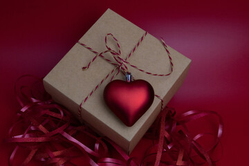 Red Heart Hanging on Craft Gift Box , surrounded with Red Ribbon on Red Background