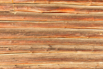 The texture of brown weathered wooden logs stacked tightly together in a bright sun.
