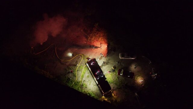Aerial footage of group firefighters putting out burning fire with trucks and smoke. City safety. Incident. Movie scene. Night cityscape.