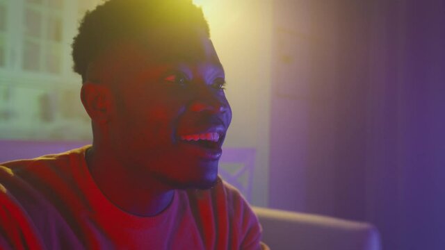 Exciting digital tv. Young amazed emotional african american guy watching tv at home in neon evening lights, empty space