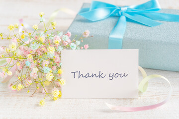 パステルカラーのカスミソウとブルーのラッピングのプレゼントと「Thank you」カード