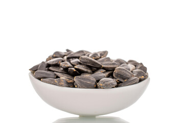 Many fragrant sunflower seeds with a white ceramic saucer, close-up, isolated on white.