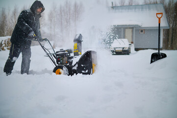 Man Removing Snow before country house with Snow-removal machine
