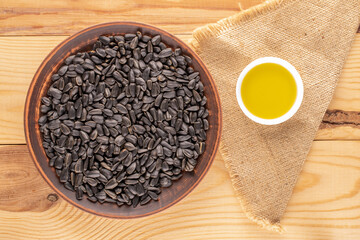 Many delicious sunflower seeds with a dish of clay and a saucer with sunflower oil on a wooden table, close-up, top view.