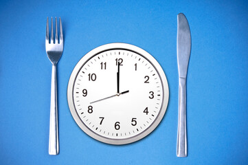 fork and knife with a clock at noon between, time for lunch and fasting concept
