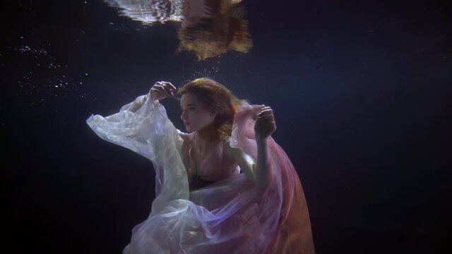 romantic nymph of lake or sea is swimming alone in dark depth, slow motion underwater shot