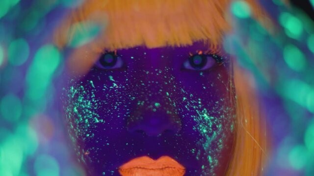Fashion model in neon lights. Close up portrait of young asian lady with bright fluorescent makeup posing to camera