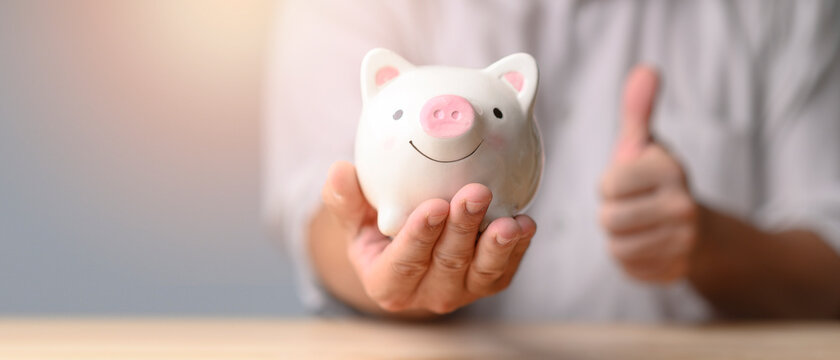 Panoramic image, Man hand holding piggy bank on wood table. Save money and financial investment. Business finance and saving money investment concept,