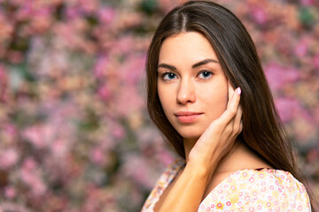 Fototapeta premium Young beautiful woman portrait. The female, the girl smiles, looks to the side on a pink with flowers background. Copy space for billboard, Beauty and freshness of spring