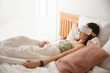 relax and massage. healthcare and medicine concept. woman uses electric eye massage machine lying in bed at home 