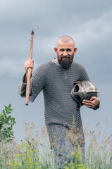 Man in medieval clothes . Viking armor. Metal helmet and chain mail.Threatens with an ax. Dark gray...