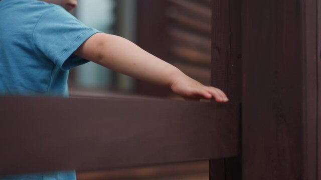 Toddler boy touches wet beam of handrail walking on veranda