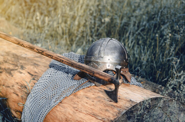 Metal chain mail, helmet and ax lie on a wooden log. Viking armor. Historical film concept.