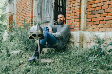 Rest of Viking warrior near an old brick castle and  trees. Sword and helmet. Pensive look. Old wooden door.