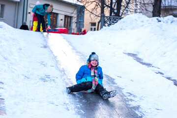 Fototapeta na wymiar little boy rides an ice slide in the city. child in blue clothes having fun and resting on winter holidays in the city
