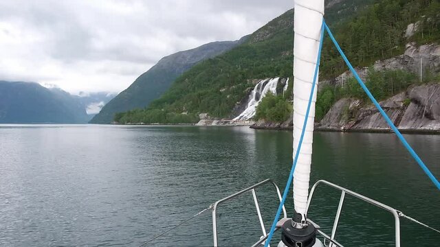 Yacht sails sea bay to hills with The Furebergfossen Waterfall on nasty day