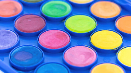 Palette of watercolor paints macro photography. Multicolored paints close-up on a blue background. The concept of developing creative skills, the ability to paint in watercolor painting courses.