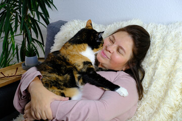 close-up of adult domestic cat, middle-aged woman of 50 years old in pink sweater sits on sofa in...