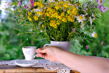 female hands holding a cup of tea, beautiful summer bouquet of wildflowers, handmade lace white...