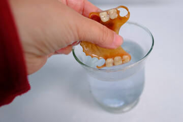 close-up partial plastic prosthesis for the upper jaw of a person in glass, disinfecting soluble effervescent tablet lies in water, air bubbles rise