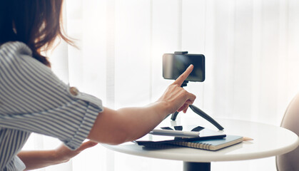 Focus on hand young asian touching on screen of mobile while she work or study online with  mobile phone on small tripod to live streaming, concept working with new normal and social distancing