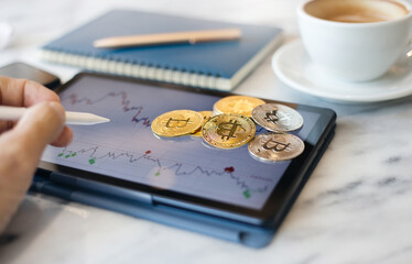 Focus on golden bitcoin on digital tablet with chart on screen and hand holding stylus pen pointing on screen, Concept invest in cryptocurrency