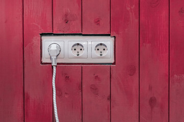 Fototapeta na wymiar Connect the power and energy plug cable to the outlet on the red wooden wall surface