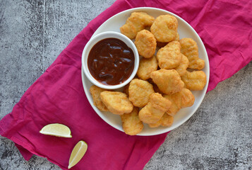 Plate full of crispy chicken nuggets with BBQ sauce and lime wedges